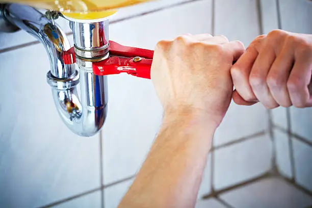 Plumber fixing leaking sink in bathroom